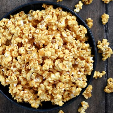 Looking down on a large bowl of caramel popcorn with spilled popcorn, honey and lemon rinds in the background.