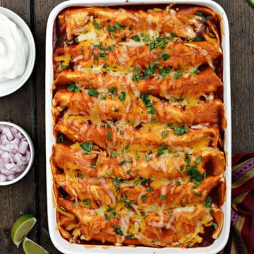 Looking down on a pan of turkey enchiladas with bowls of sour cream, red onion, cilantro, and avocado chunks around the edge.