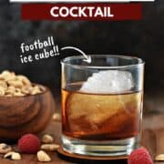 A peanut butter whiskey cocktail in a short glass with a football shaped ice cube and wooden bowl of peanuts in the background and title graphic across the top.
