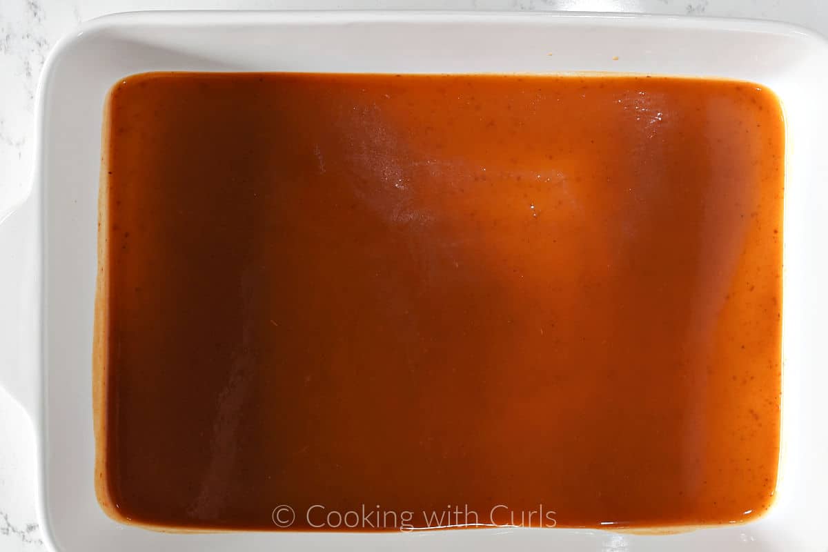 Red enchilada sauce coating the bottom of a baking dish. 