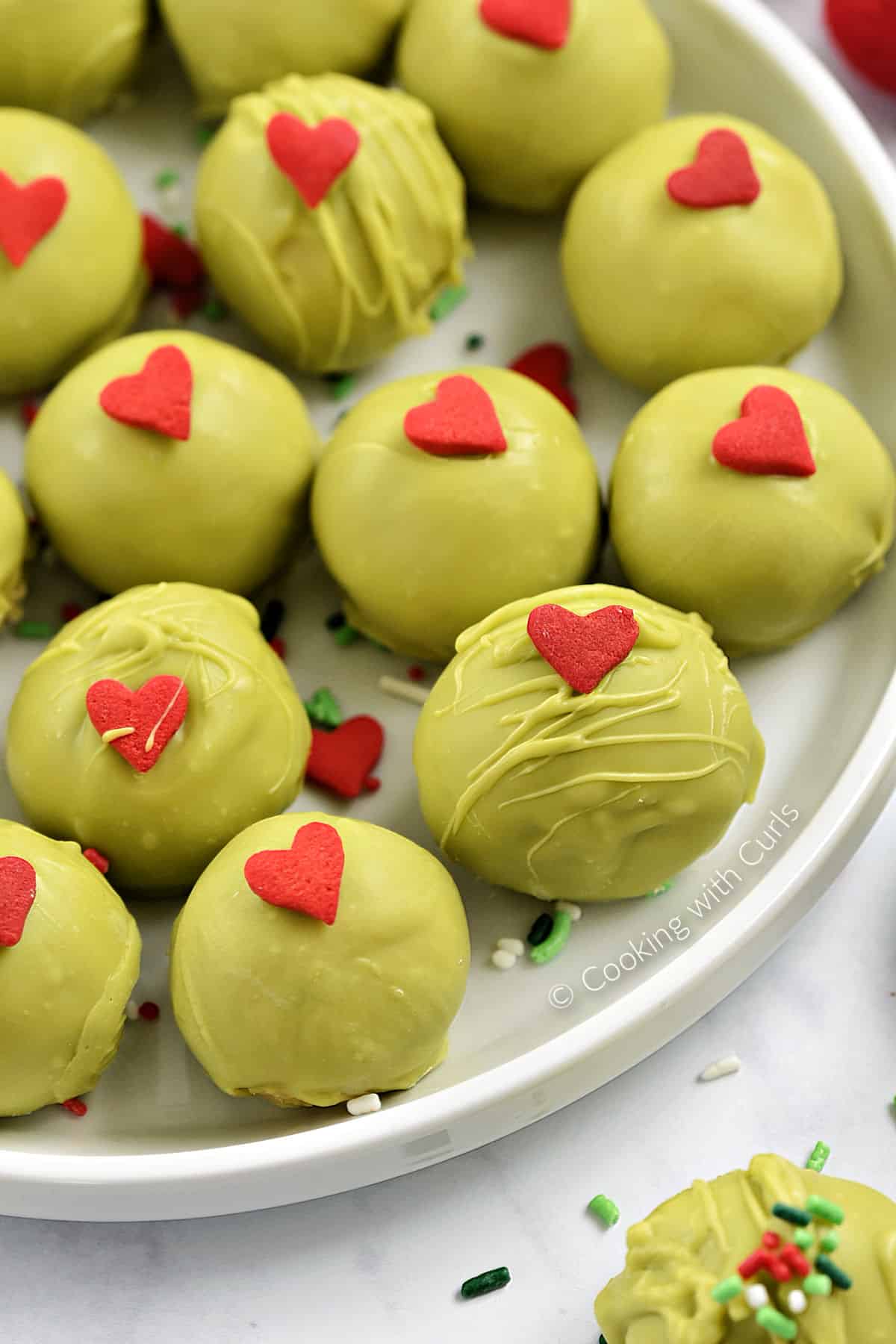 Thirteen green chocolate covered cookie balls with red candy hearts on a plate. 