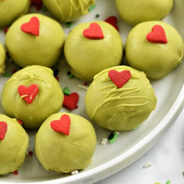 Thirteen green chocolate covered cookie balls with red candy hearts on a plate.