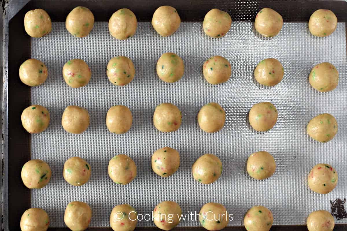 Thirty-five rolled cookie balls on a silicone lined baking sheet. 