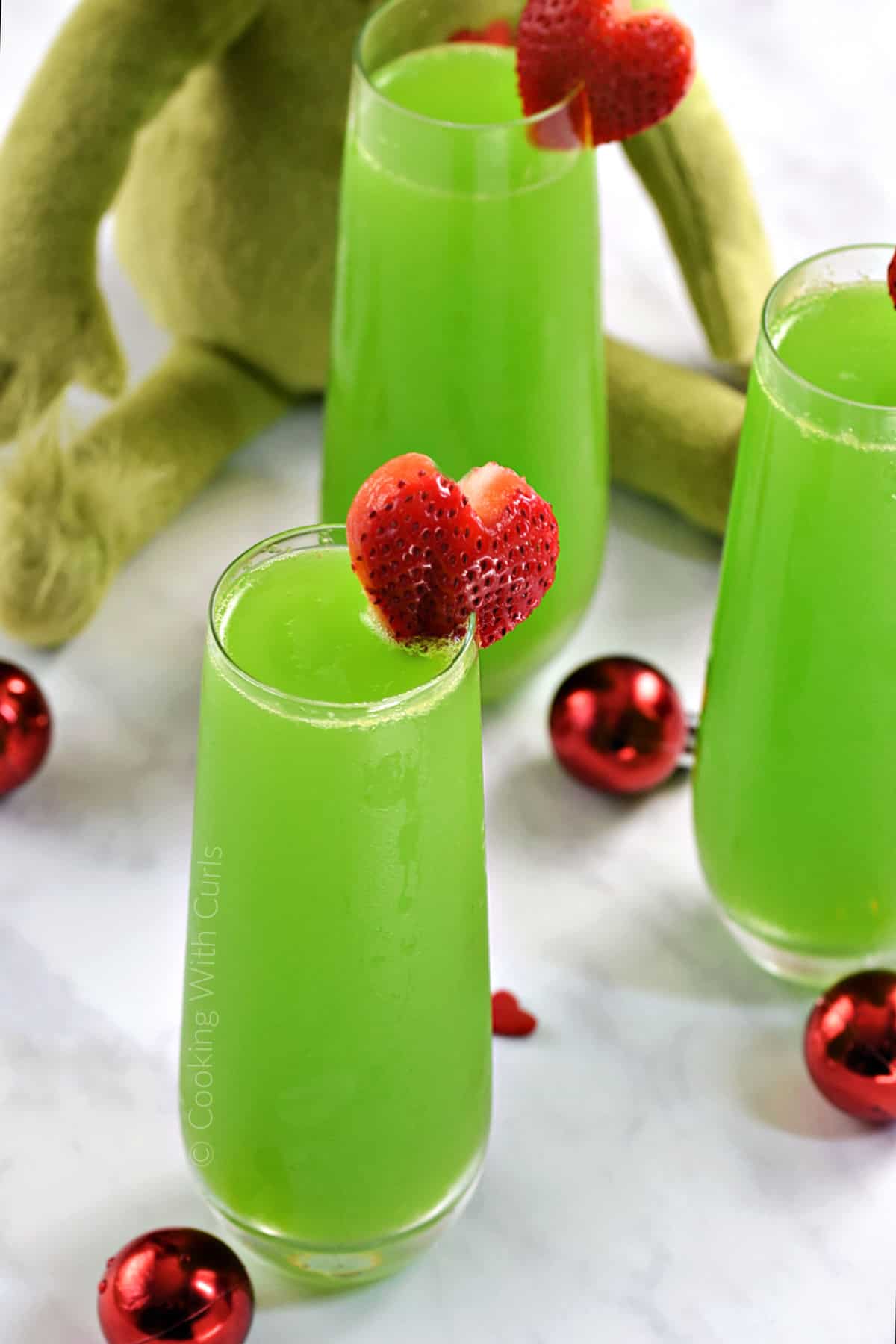 Three tall glasses of bubbly green cocktails with a strawberry shaped heart on the rim. 