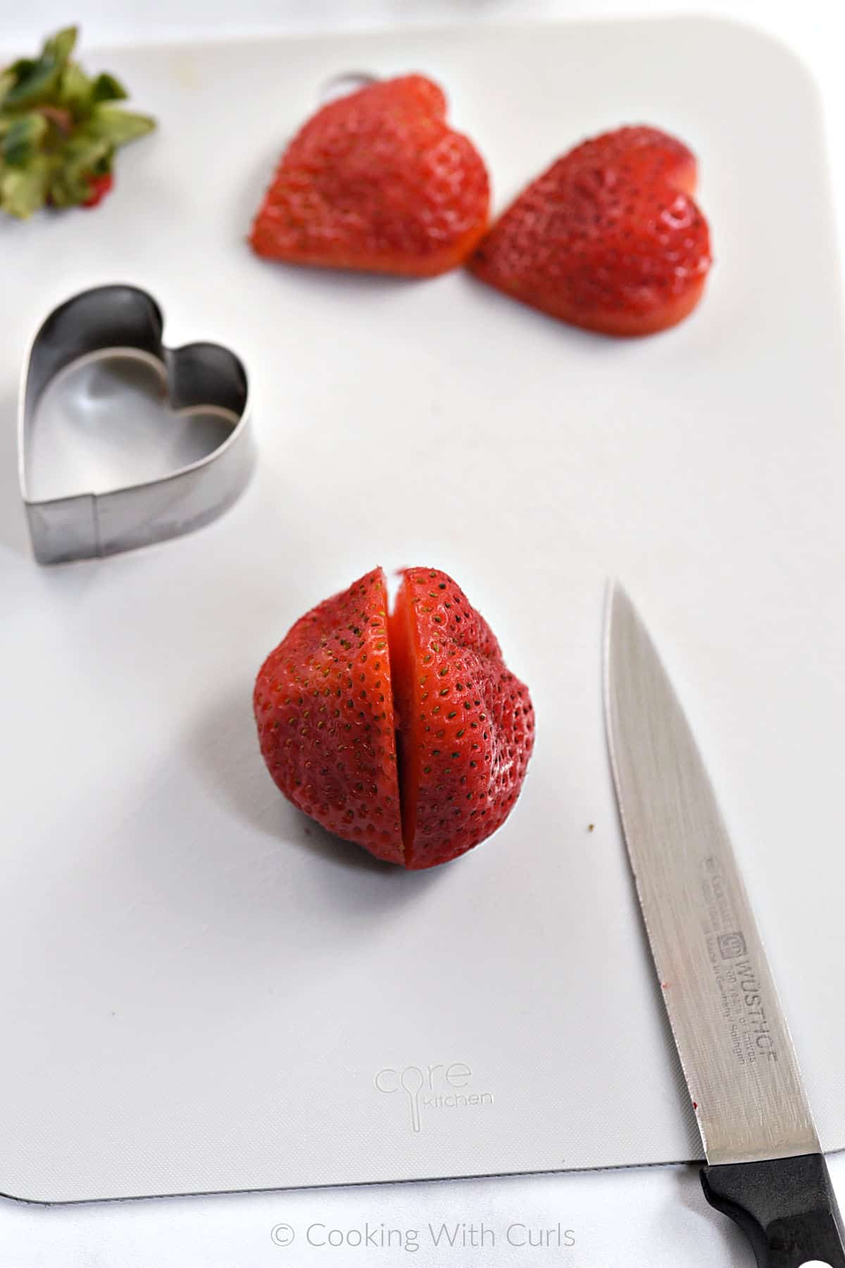 Two large strawberries cut in half on a cutting mat. 