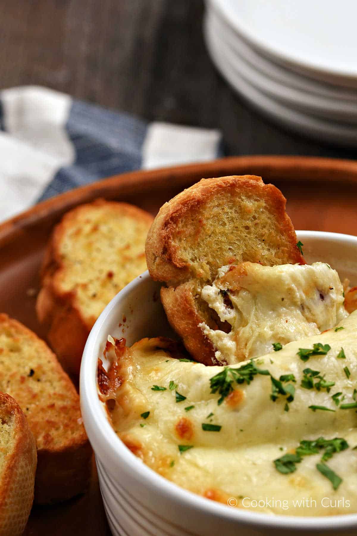 An air fryer crostini in a bowl of cheesy dip with three more baguette slices on the side. 