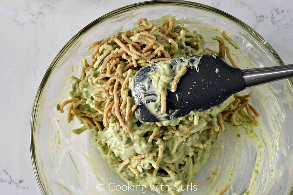 Chow mein noodles and chopped pistachios mixed with melted green chocolate in a large mixing bowl. 