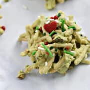 Close-up image of a green chocolate covered Grinch Haystack Cookies with a red heart and holiday sprinkles.