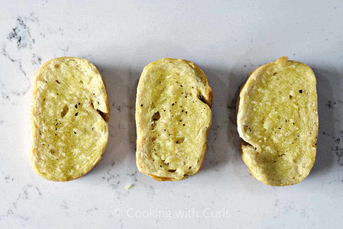 Three slices of baguette topped with olive oil, salt and pepper. 