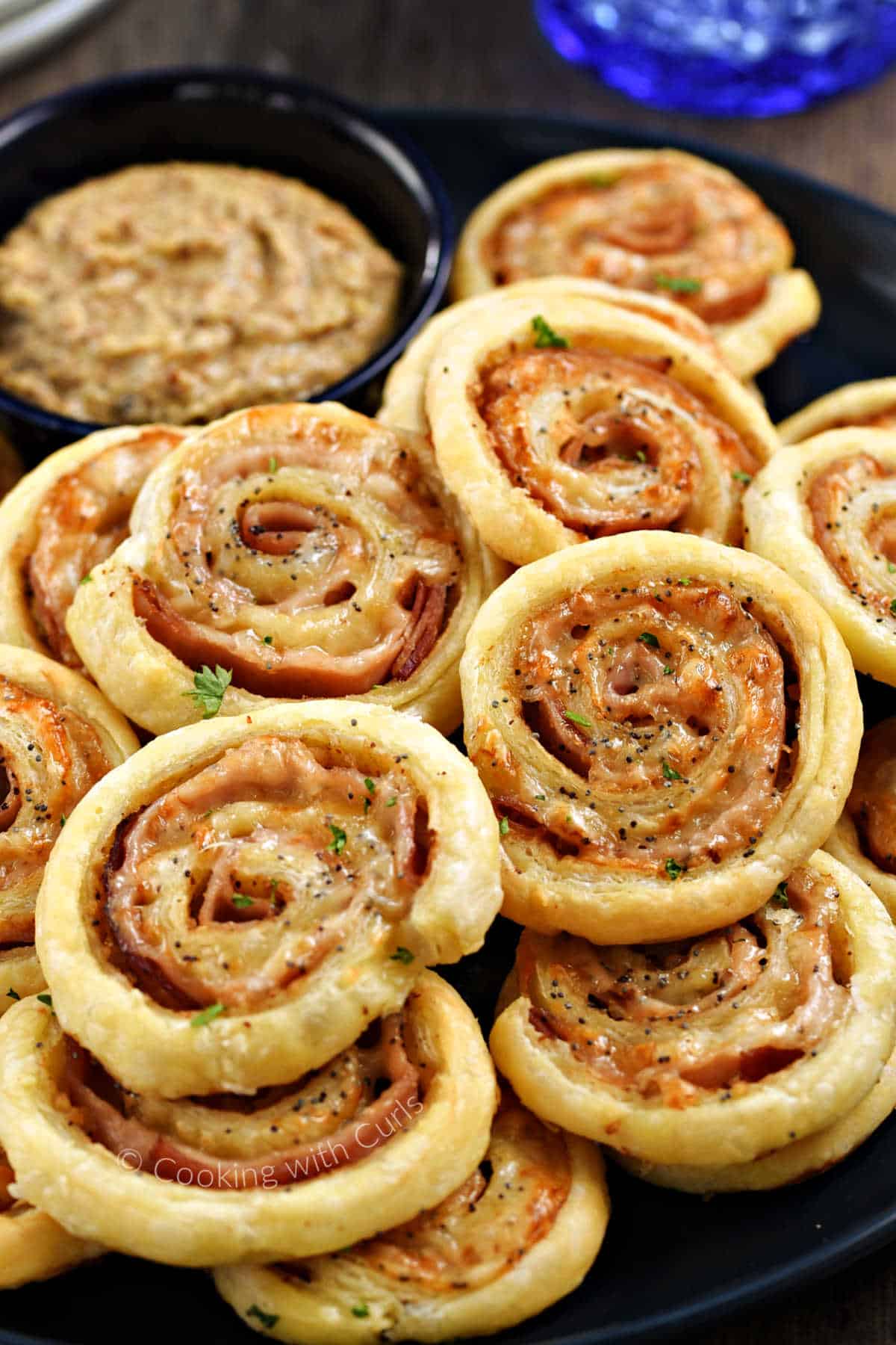 Ham and cheese pinwheels stacked on a plate with a bowl of mustard in the background.