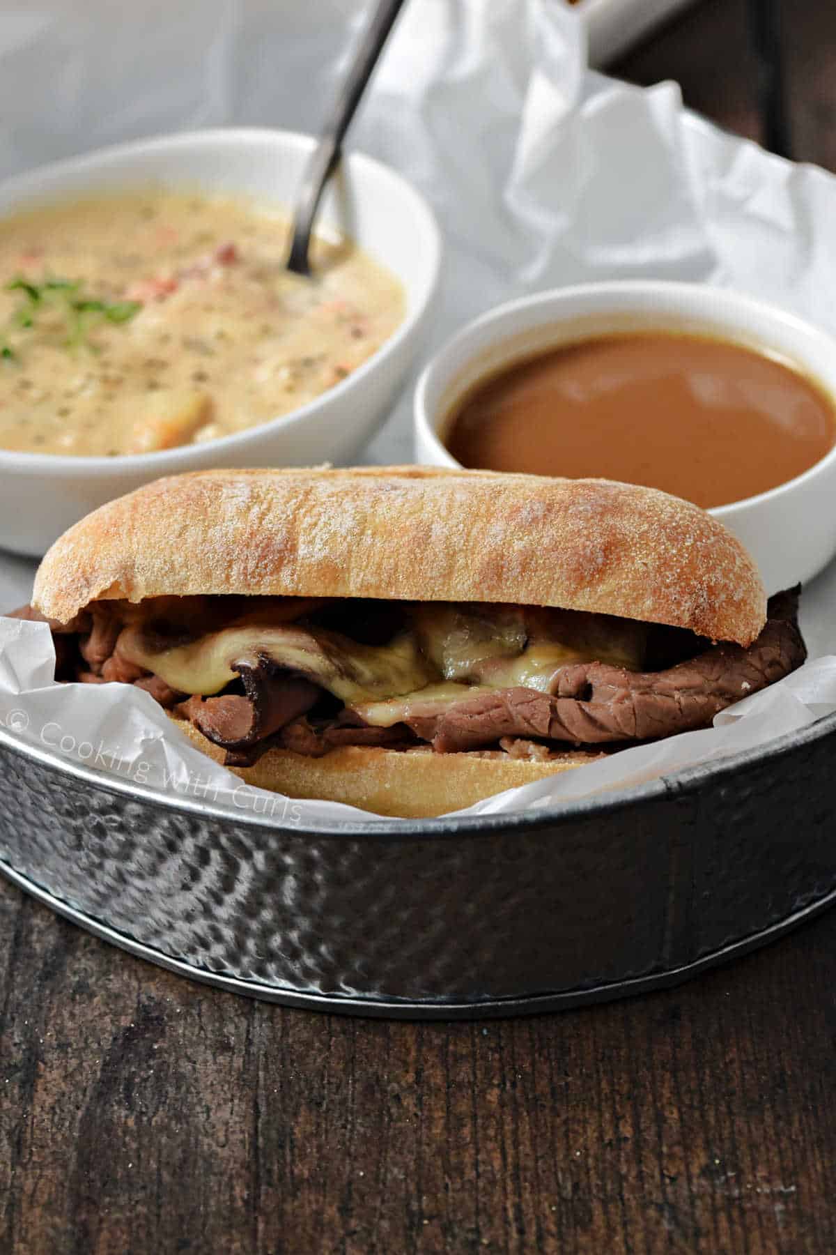 French Dip Sandwich with melted cheese served with a small cup of au jus and a bowl of New England clam chowder. 