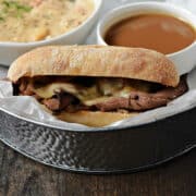French Dip Sandwich with melted cheese served with a small cup of au jus and a bowl of New England clam chowder.