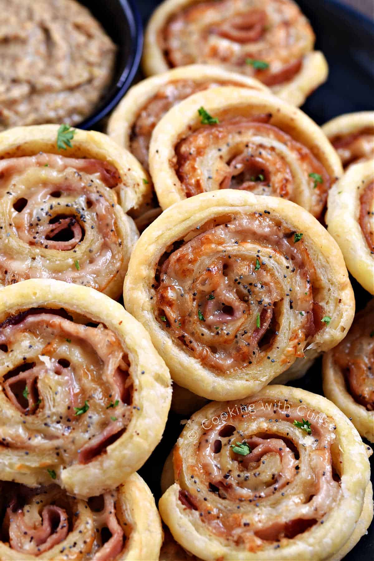 Ham and cheese pinwheels stacked on a plate with a bowl of Dijon mustard in the background.