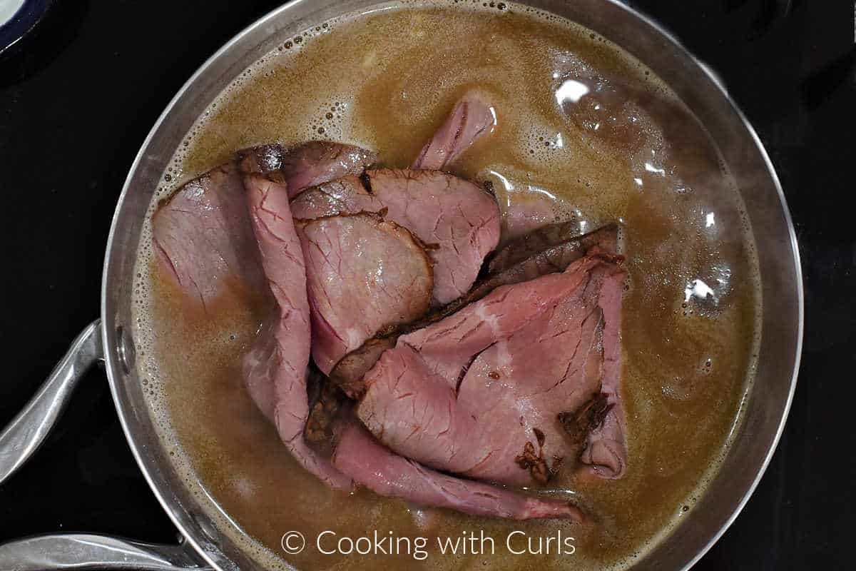 Sliced roast beef in a saucepan of simmering au jus. 
