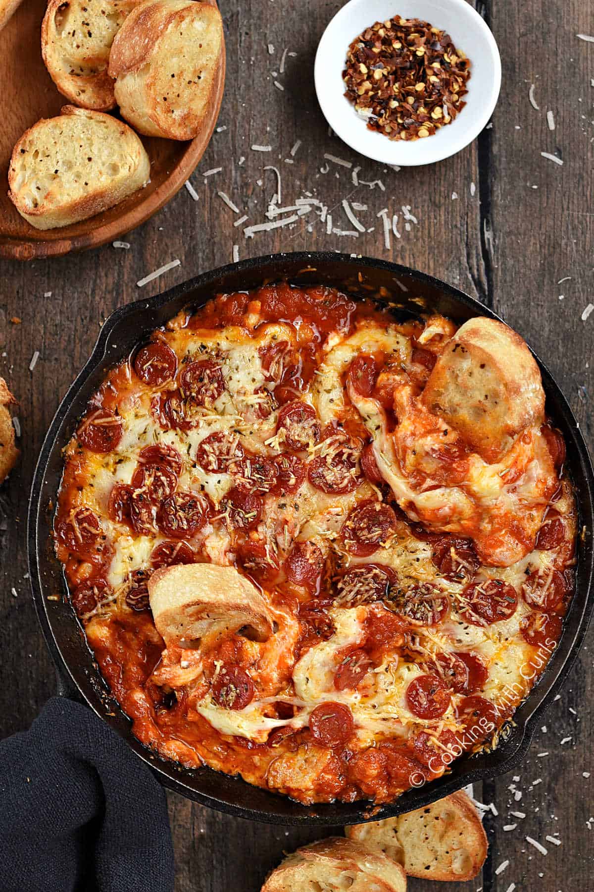 Looking down on cheesy pizza dip in a cast iron skillet with two toasted baguette slices dipped into the edge.