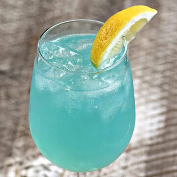 Teal blue dream sangria cocktail with ice cubes in a wine glass with a lemon wedge on the rim.