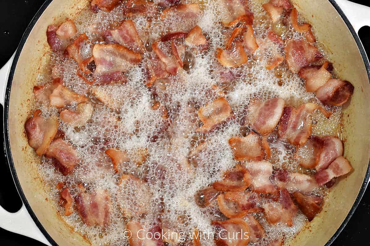Chopped pieces of bacon simmering in a large cast iron skillet.
