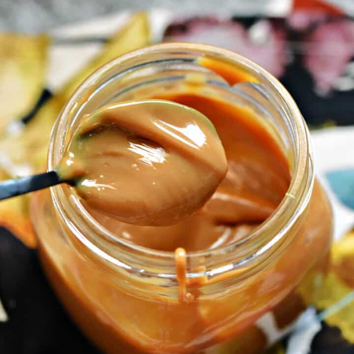 Instant pot Dulce de Leche in a jar with a caramel filled spoon on the edge.