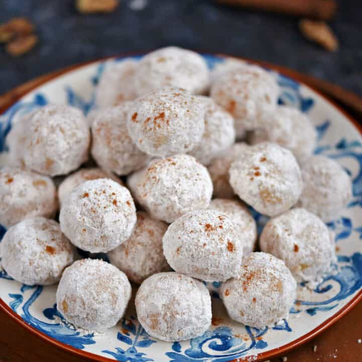 A plate filled with round, powdered sugar covered snowball cookies.