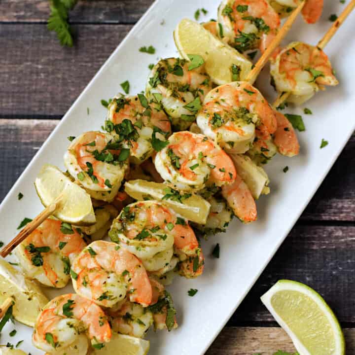 Skewered cilantro lime shrimp on a platter sprinkled with chopped cilantro.