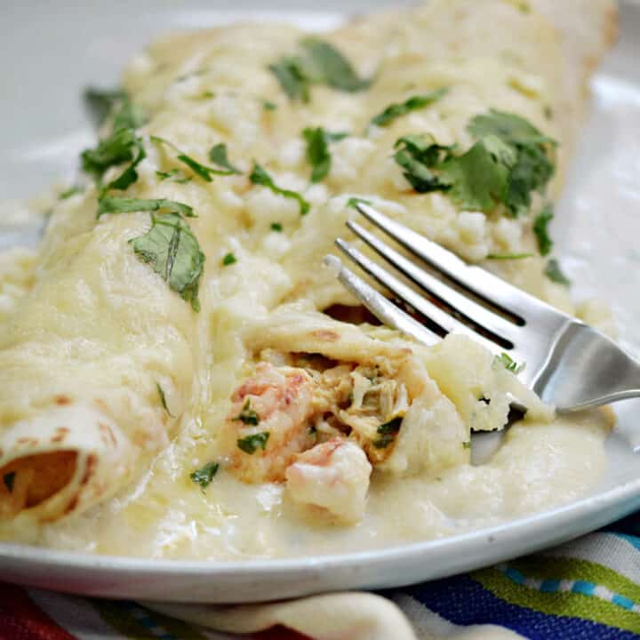 Two creamy seafood enchiladas on a plate garnished with chopped cilantro.