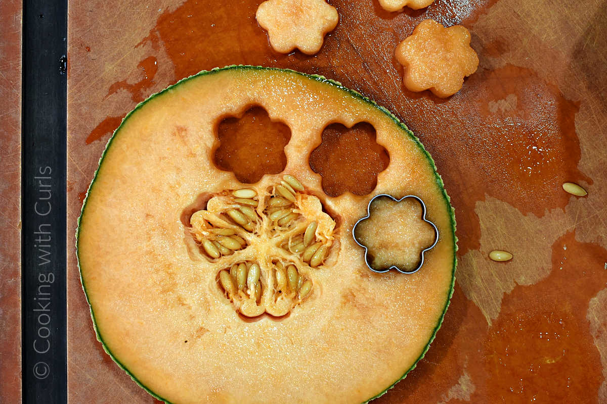 Flower shapes cut into a slice of cantaloupe melon on a cutting board.