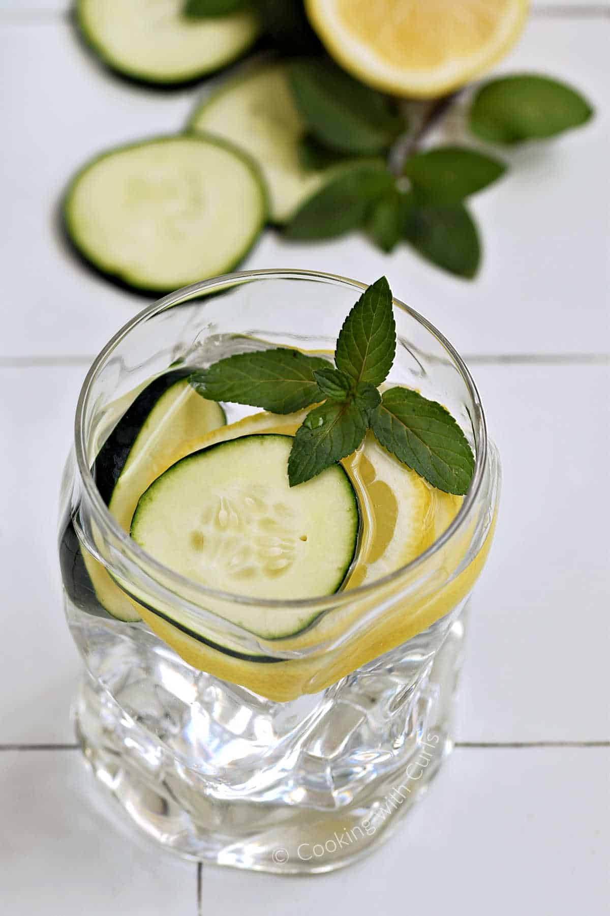 A glass of water with cucumber and slices topped with a mint sprig.
