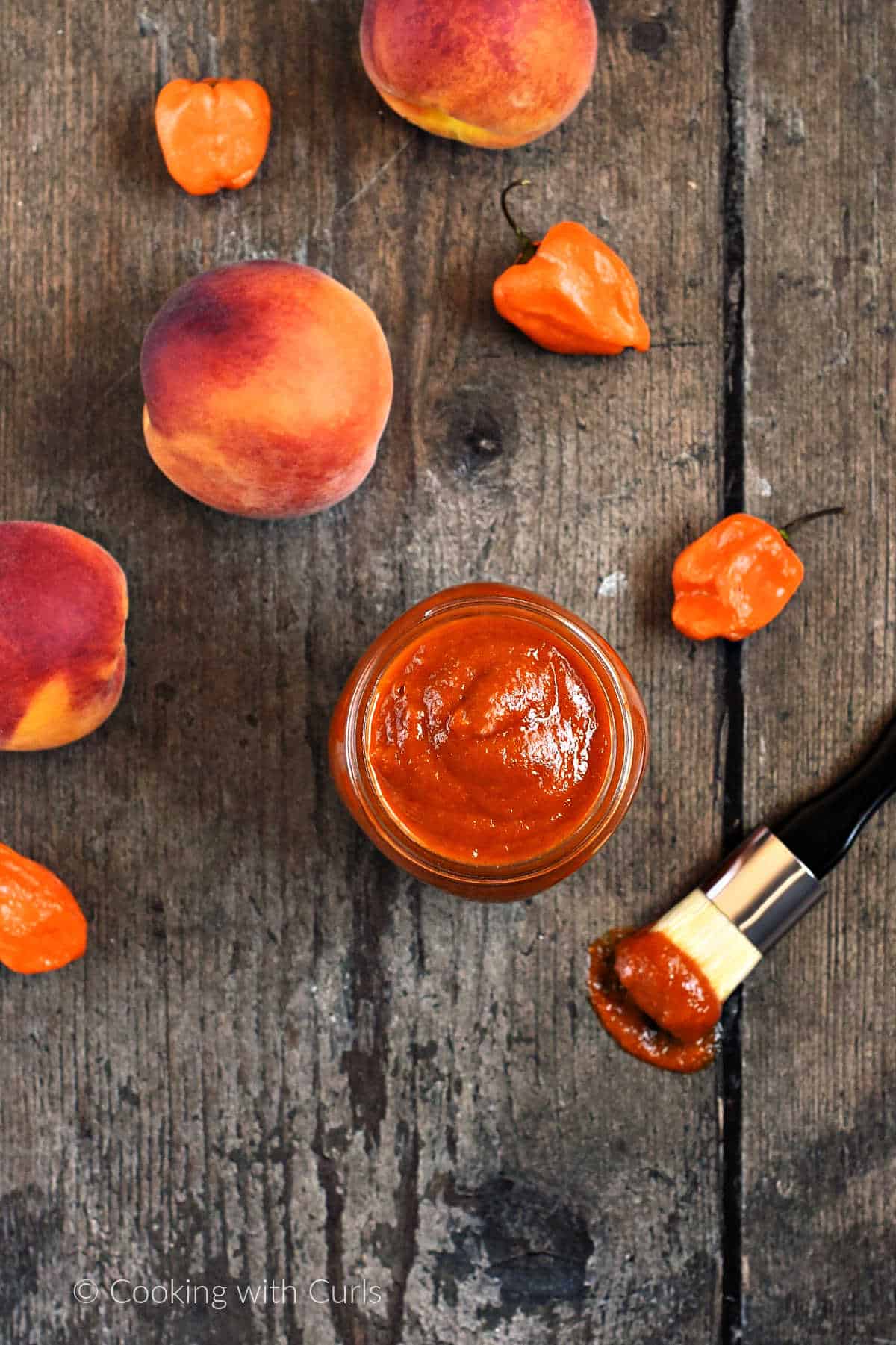 Looking down on a jar of peach habanero barbecue sauce surrounded by peaches and orange peppers.