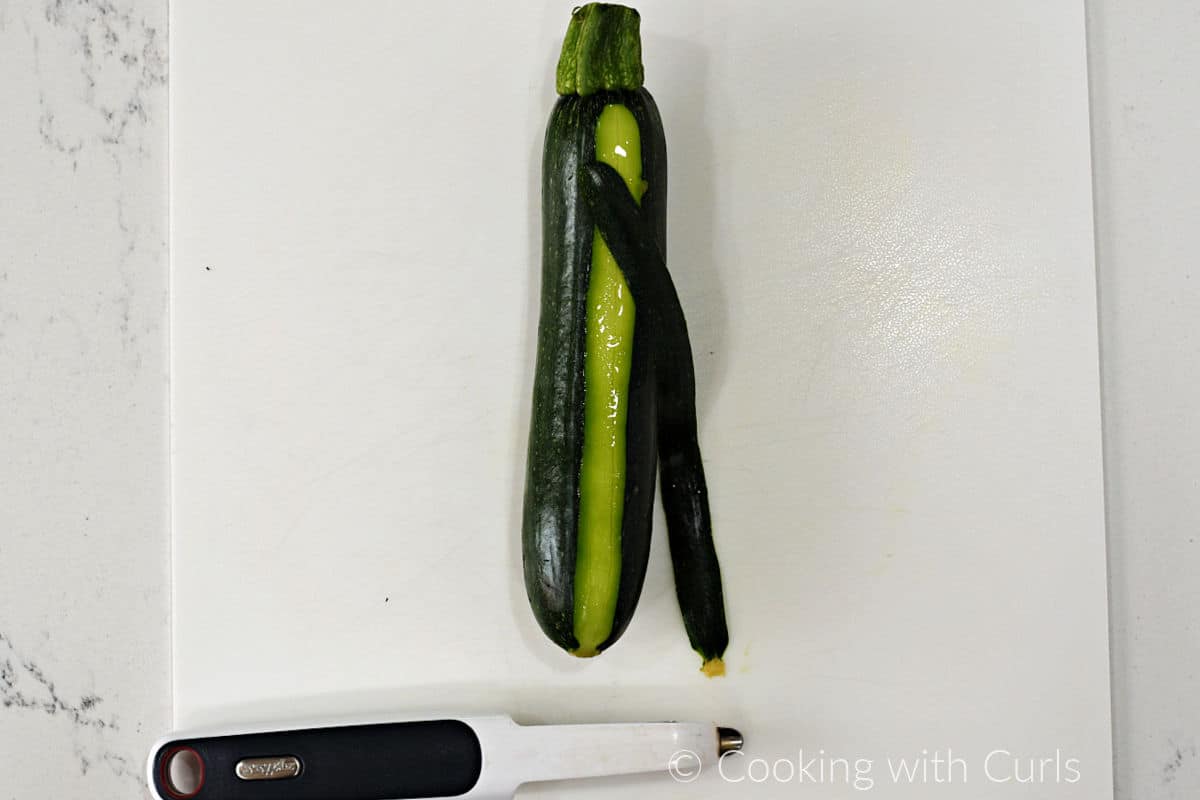 A zucchini with a slice of skin removed with a vegetable peeler.