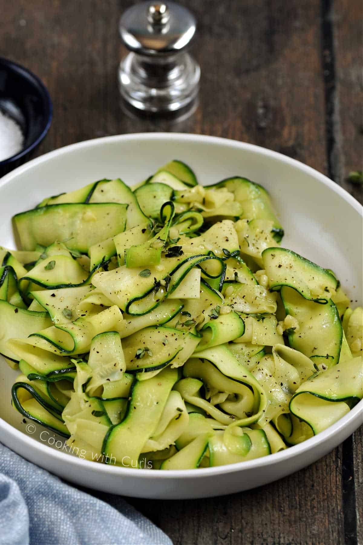 A bowl of easy sauteed zucchini ribbons sprinkled with pepper and fresh thyme leaves.