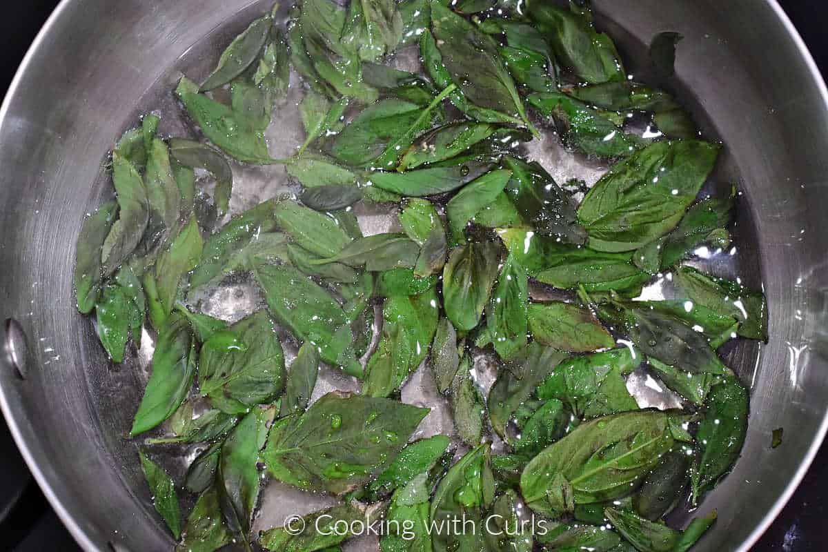 Basil leaves, water, and sugar simmering in a saucepan.