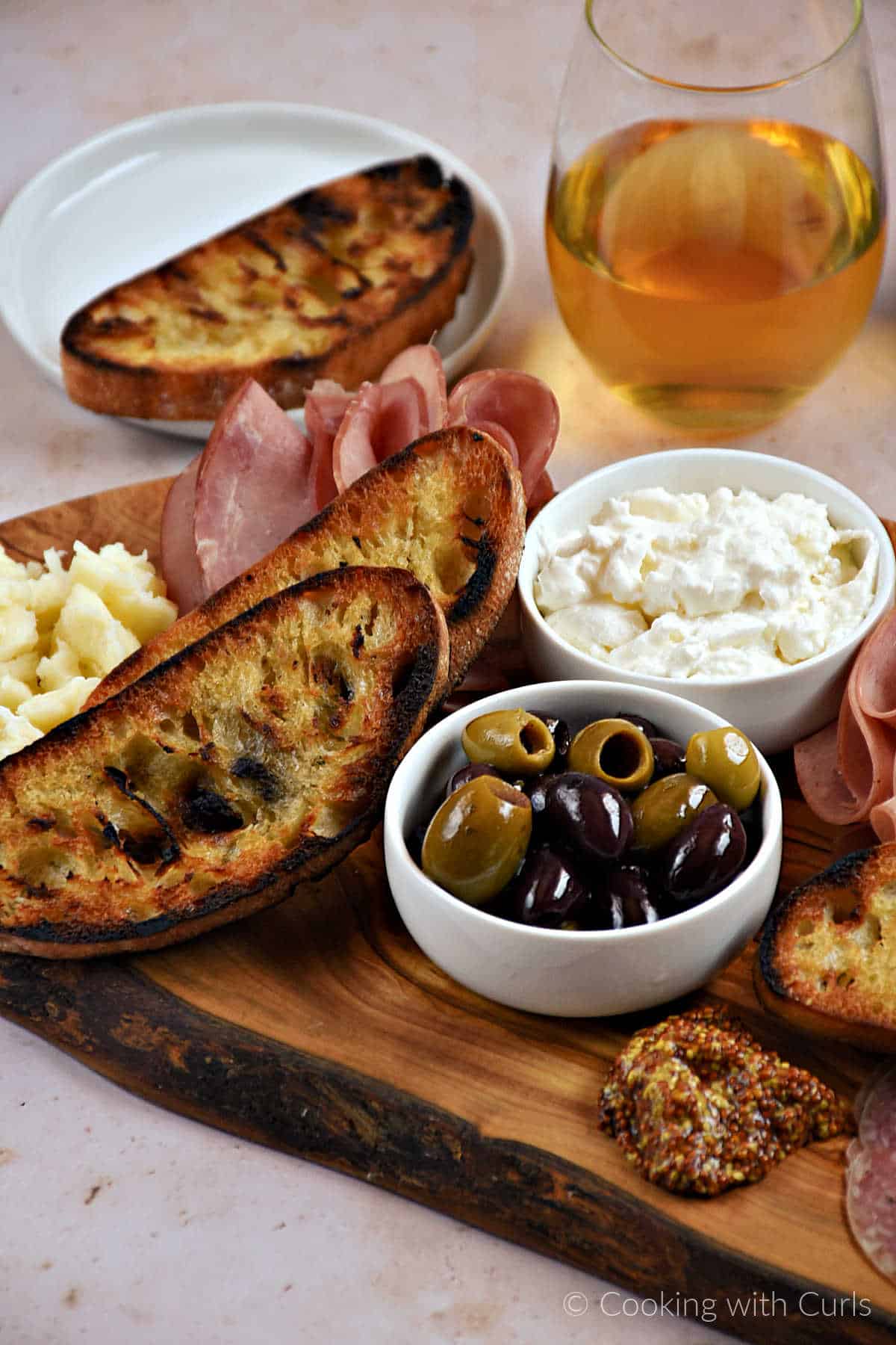 Mozzarella cheese, ham, olives, mustard, and bowl of burrata cheese on a wood board.