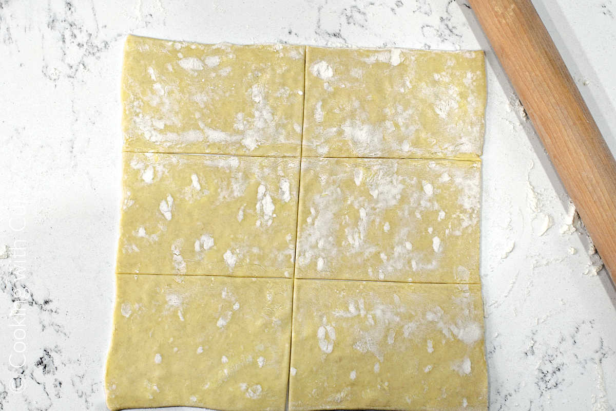 A puff pastry sheet on a floured work surface cut into six rectangles.