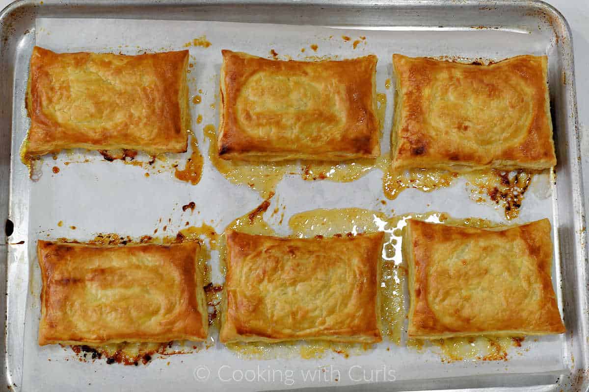 Six baked puff pastry tarts upside down on a parchment lined baking sheet.