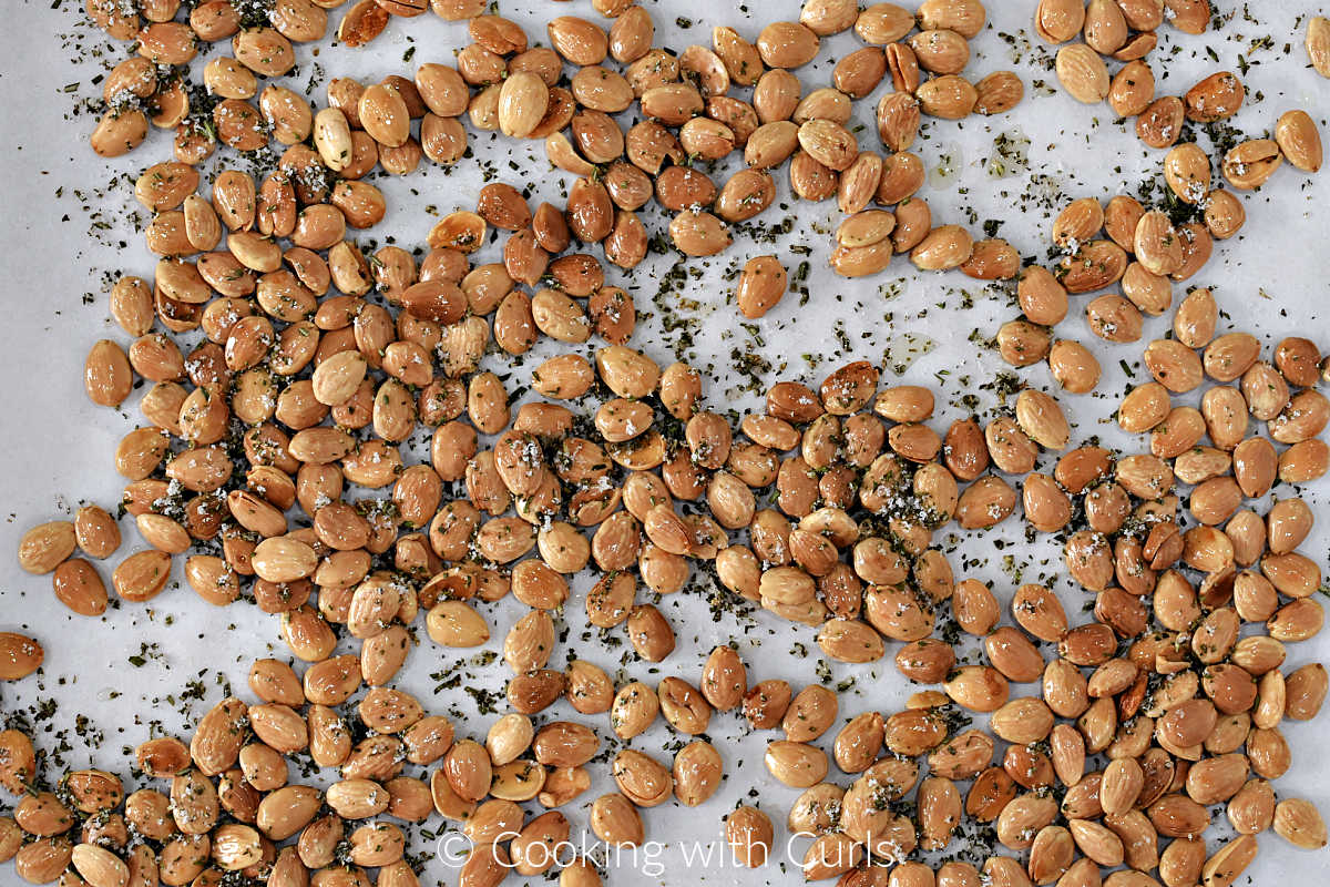 Roasted almonds tossed with chopped rosemary and sea salt on a parchment lined baking sheet.