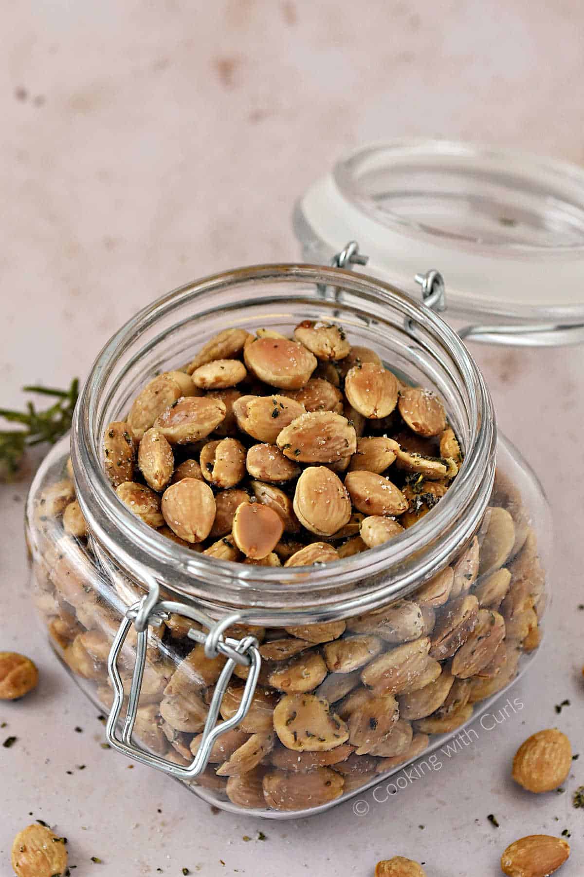 A lidded jar filled with roasted Marcona almonds tossed in sea salt and chopped rosemary.
