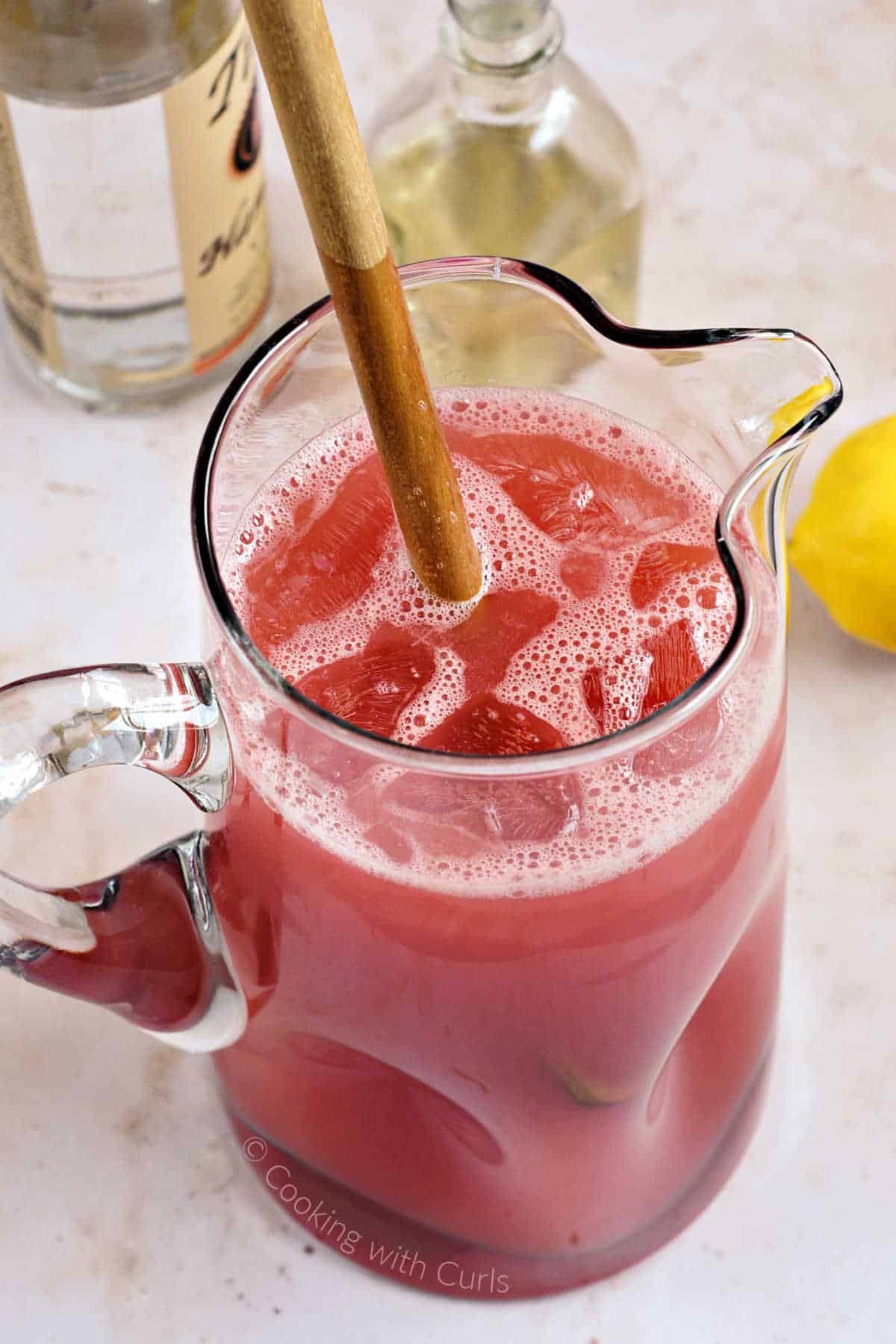 Watermelon basil lemonade in a large pitcher mixed with a large wooden spoon.