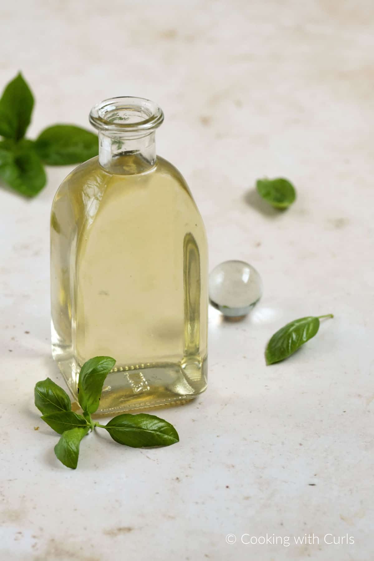 Basil simple syrup in a glass bottle surrounded by basil leaves.