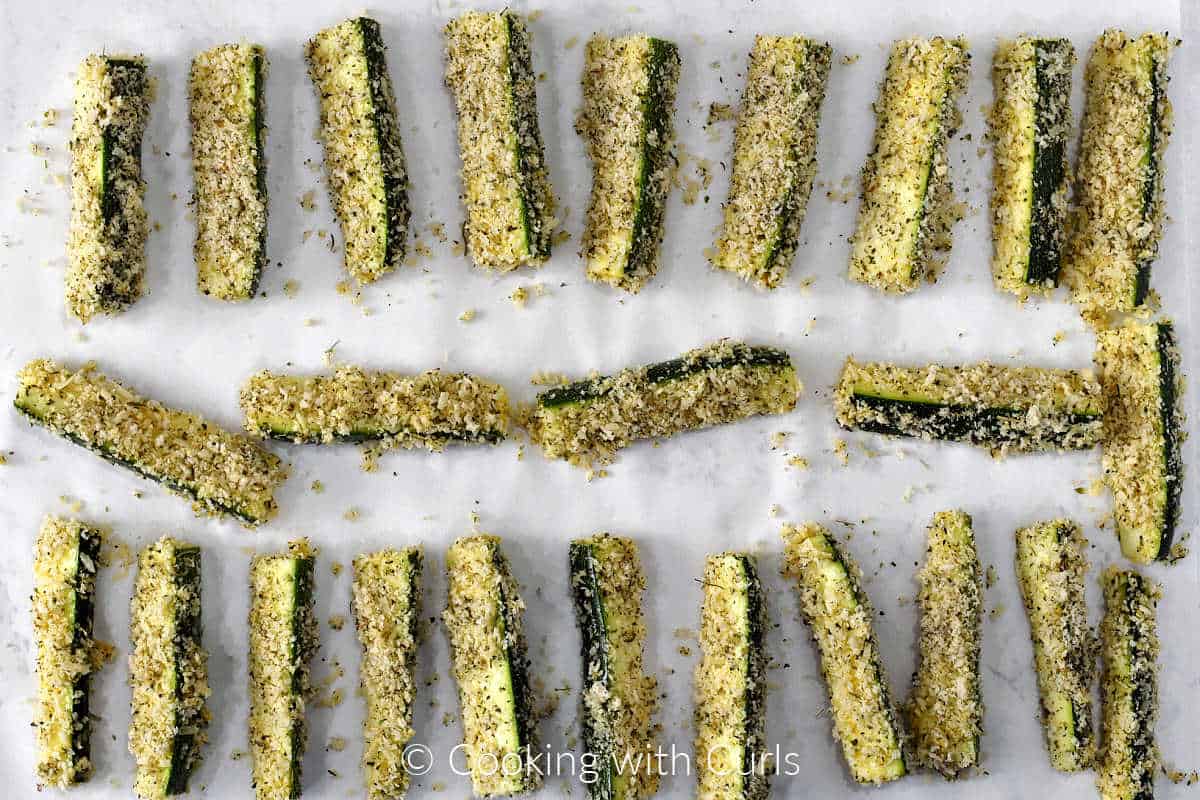 Breaded zucchini sticks lined up on parchment paper.