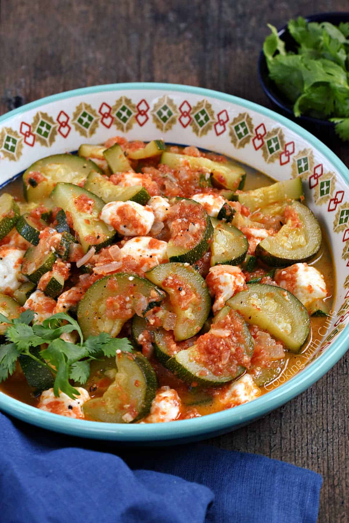 A bowl of half rounds of zucchini and chunks of cheese in a tomato sauce.
