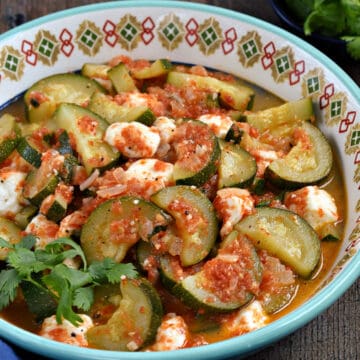 A bowl of half rounds of zucchini and chunks of cheese in a tomato sauce.