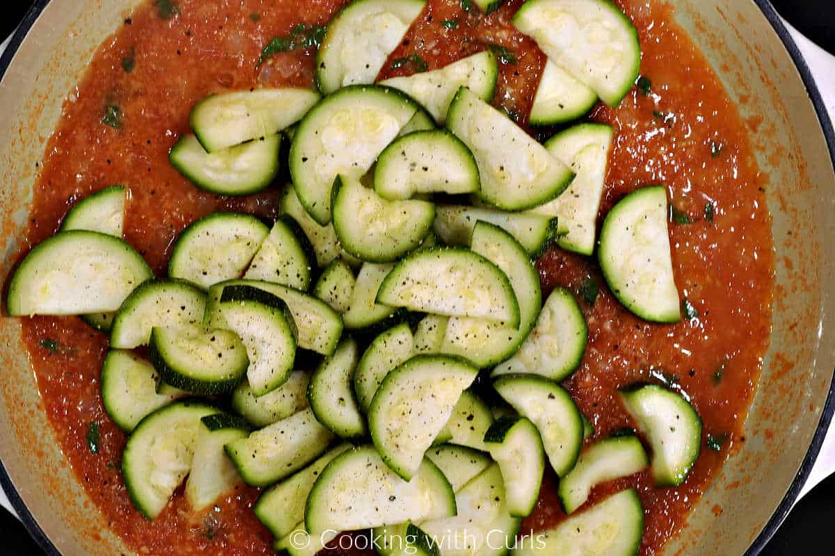 Zucchini slices added to the tomato sauce in a skillet.
