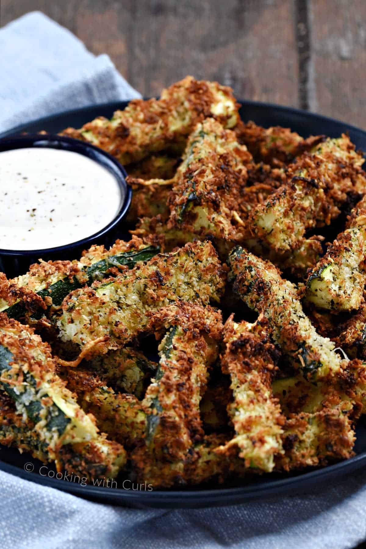 A plate filled with crispy zucchini fries with a small bowl of ranch dressing.