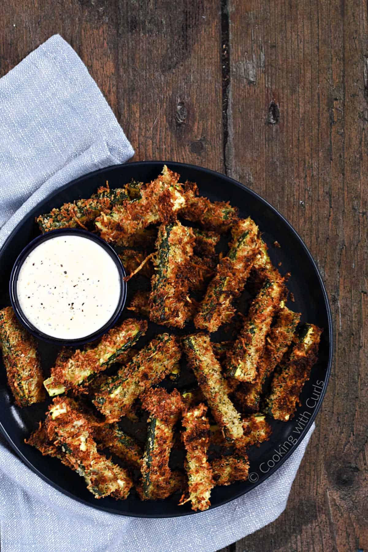 Looking down on a plate of crispy zucchini fries with a side of ranch dressing.