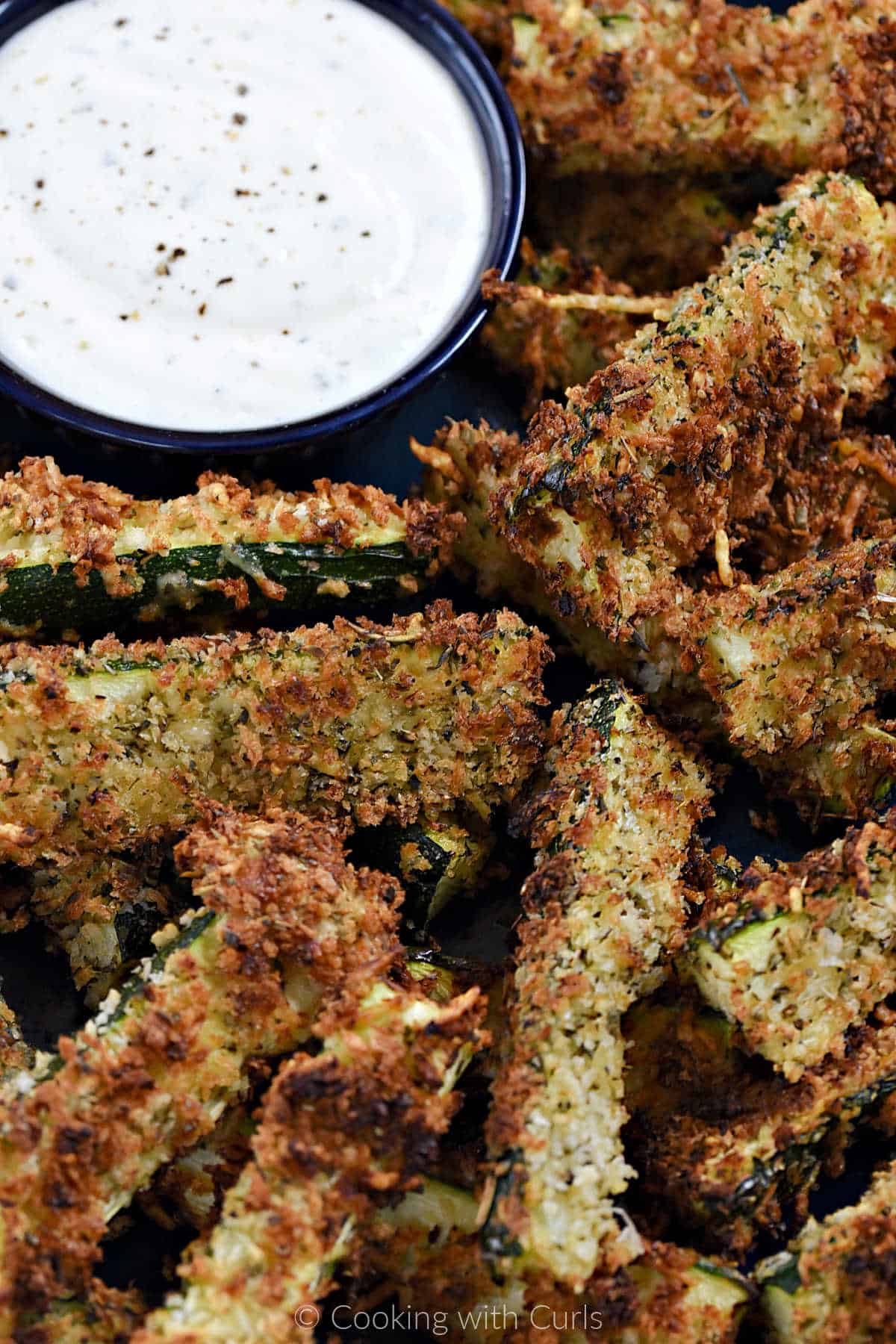 Close-up image of crispy zucchini fries with a small bowl of ranch dressing.