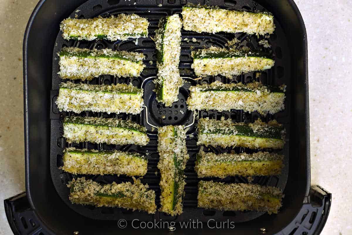 Fourteen coated zucchini sticks in an air fryer basket.