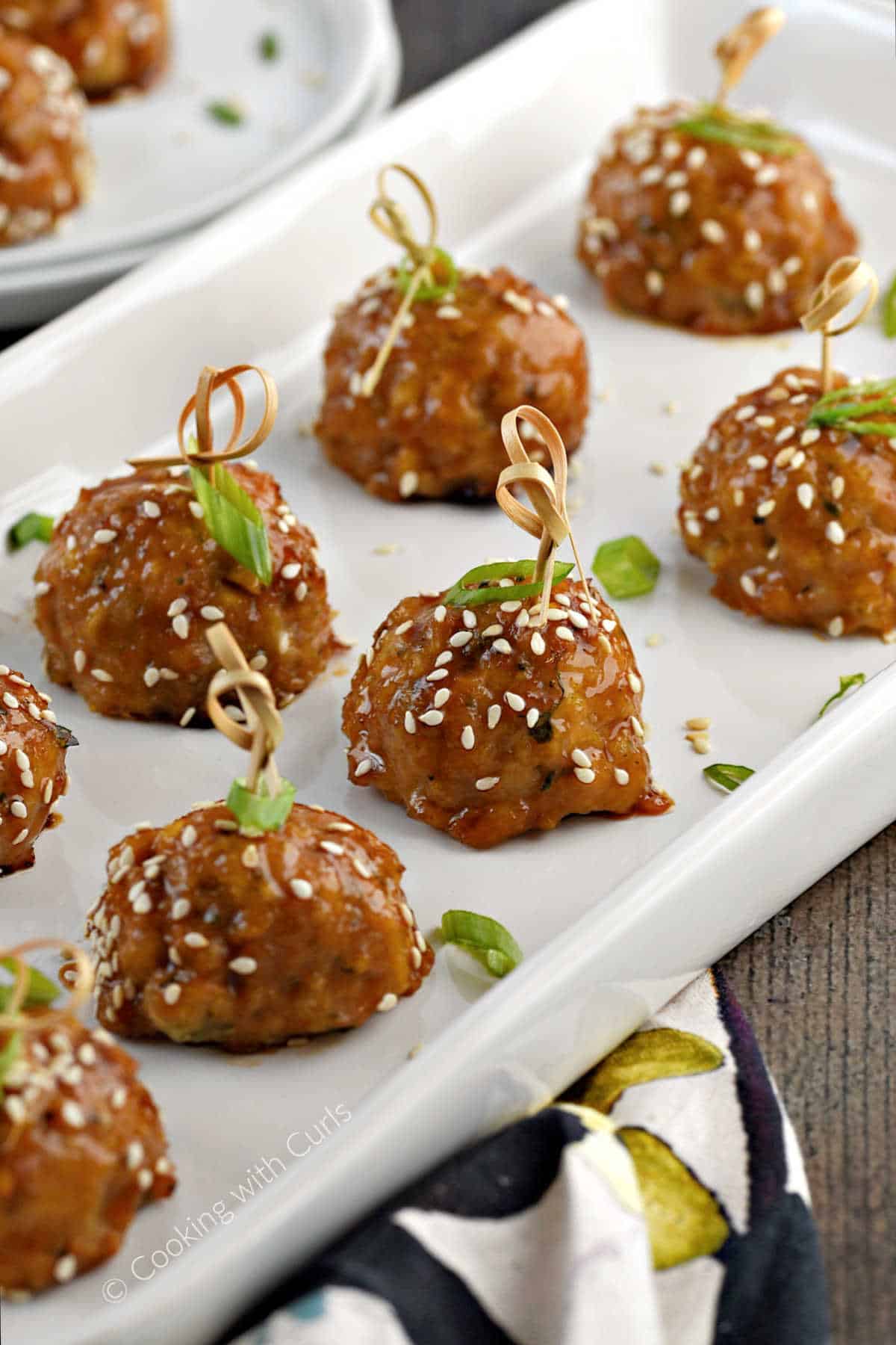 Chicken teriyaki meatballs on a platter with sesame seeds and green onion slices.