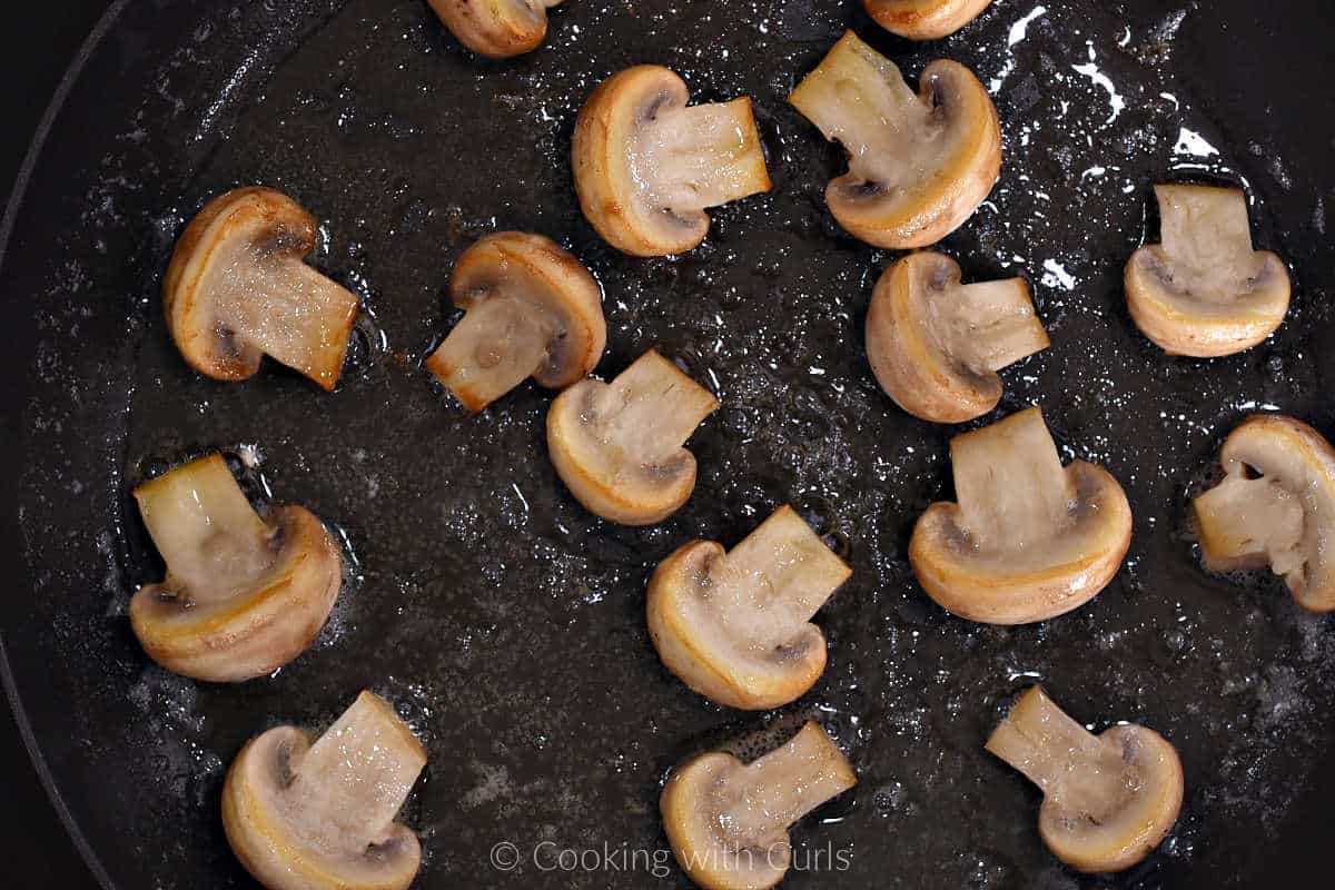 The cut side of mushroom halves cooking in a non-stick skillet with butter and oil.