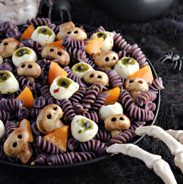 Black spiral pasta, mushroom skulls, mozzarella eyeballs, and orange triangles in a black serving bowl.
