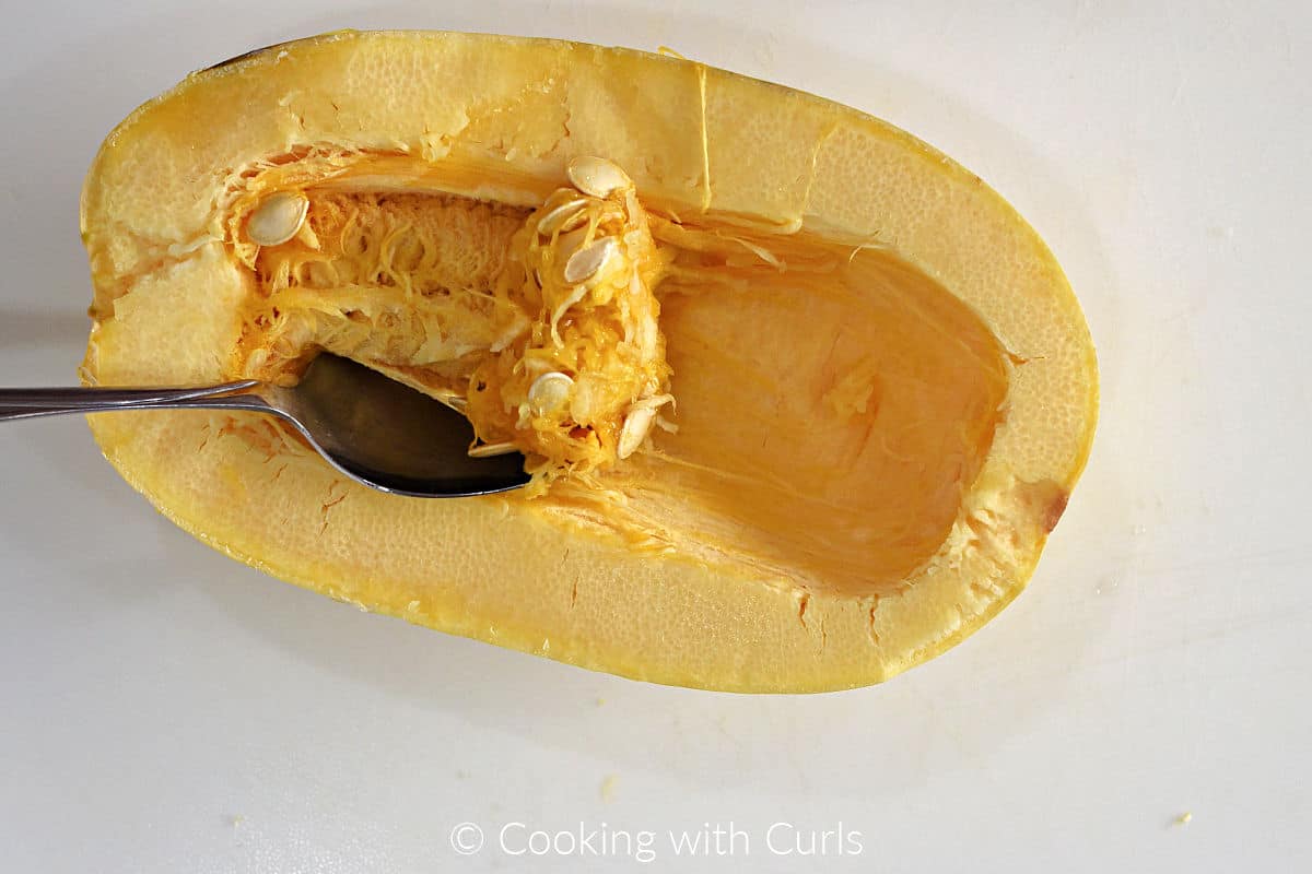 Large spoon scooping out spaghetti squash seeds and pulp.